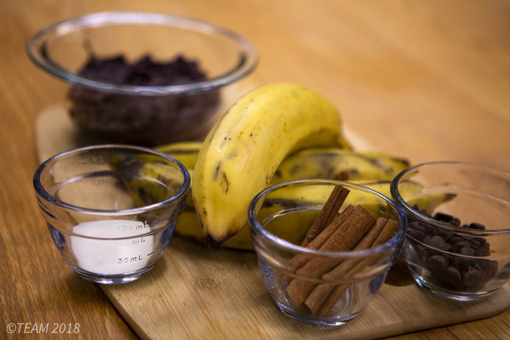 All of the ingredients are set out on a cutting board: plantains, sugar, cinnamon, chocolate, and black beans.