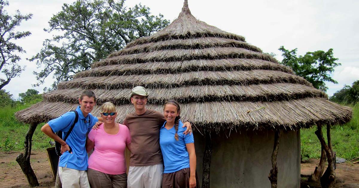 Tompkins family with legacy of faithful financial giving standing in front of hut on mission trip