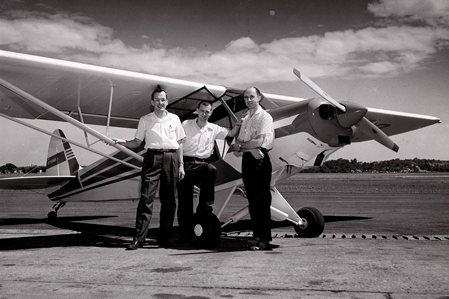 three men standing in front of a small aircraft